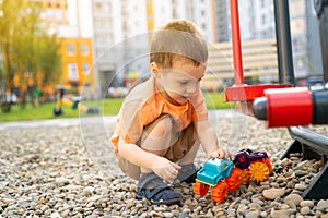 Little toddler boy playing with cars on pebbles on the playground. Boy two or three years old. Toddlerhood childhood concept.
