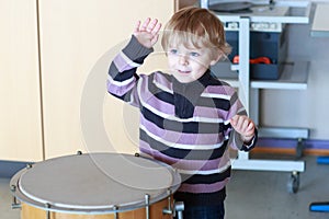 Little toddler boy playing drum at music school.