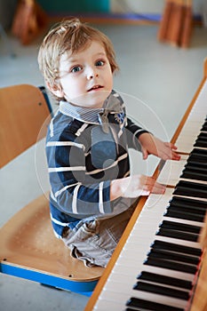 Little toddler boy playing piano at music school.