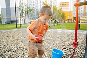 Little toddler boy playing with toys on pebbles on the playground. Boy two or three years old. Toddlerhood childhood concept.