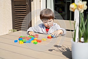 Little toddler boy playing wooden 3D puzzles on terrace outdoors