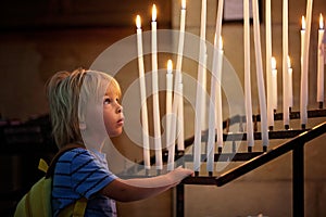 Little toddler boy, praying in chapel with candles in front