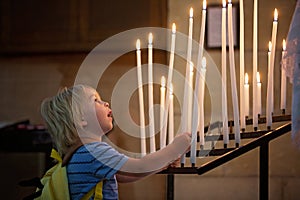 Little toddler boy, praying in chapel with candles in front