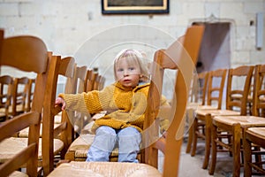 Little toddler boy, praying in chapel with candles in front