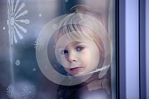 Little toddler boy, sitting behind the window