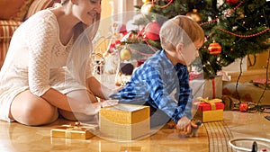 Little toddler boy sitting on floor with beautiful young mother under Christmas tree