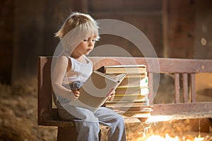 Little toddler boy, sitting on old vintage bench, holding books in attic