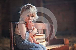 Little toddler boy, sitting on old vintage bench, holding doll  in attic
