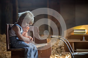 Little toddler boy, sitting on old vintage bench, holding doll  in attic