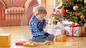 Little toddler boy sitting under Christmas tree and crying