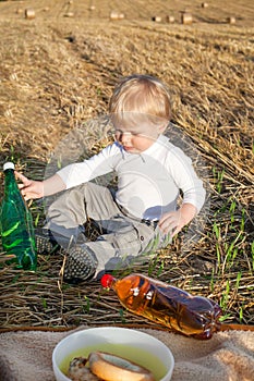 Little toddler boy of two years making picnic on golden hay field