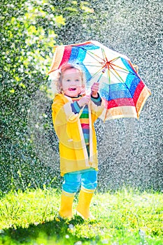 Little toddler with colorful umbrella playing in rain