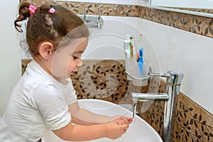 Little toddler girl in bathroom washing hands. Cute sweet baby play in water.