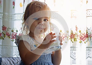 Little toddler girl child drinks from a glass goat or cow milk, natural rustic. The happy kid smiles and looks pleased