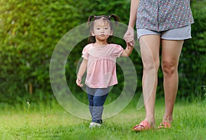 Little toddler girl holding her mother`s hand and walking in grass field