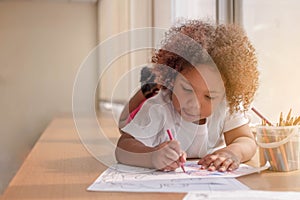 Little toddler girl laying down concentrate on drawing. Mix African girl learn and play in the pre-school class. Children enjoy