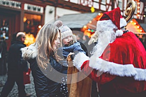 Little toddler girl with mother on German Christmas market. Happy kid taking gift from bag of Santa Claus. Smiling woman