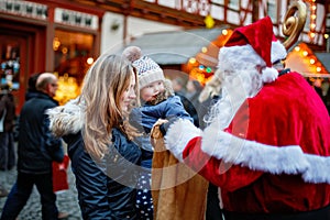 Little toddler girl with mother on German Christmas market. Happy kid taking gift from bag of Santa Claus. Smiling woman