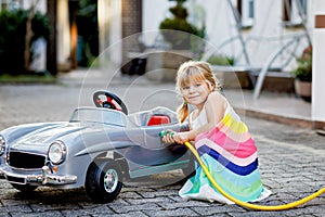 Little toddler girl playing with big vintage toy car and having fun outdoors in summer. Cute child refuel car with water