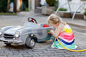 Little toddler girl playing with big vintage toy car and having fun outdoors in summer. Cute child refuel car with water