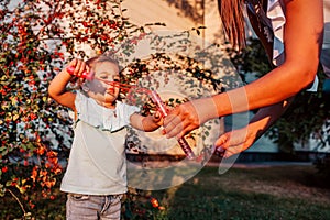 Little toddler girl playing with soap bubbles in summer park. Happy kid having fun outdoors. Mother helping daughter