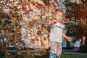 Little toddler girl playing with soap bubbles in summer park. Happy kid having fun outdoors