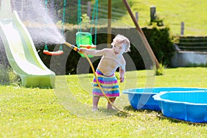 Little toddler girl playing with water hose in the garden