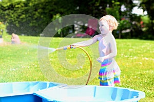 Little toddler girl playing with water hose in the garden
