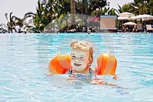 Little toddler girl with protective swimmies playing in outdoor swimming pool by sunset. Baby Child learning to swim in