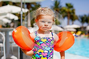 Little toddler girl with protective swimmies playing in outdoor swimming pool by sunset. Baby Child learning to swim in