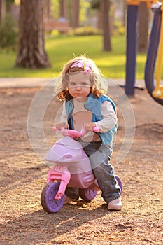 Little toddler girl riding a small pink bike in the sunlit park