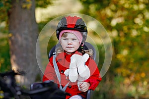 Little toddler girl with security helmet on head sitting in bike seat of her mother or father bicycle. Safe and child