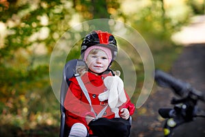 Little toddler girl with security helmet on head sitting in bike seat of her mother or father bicycle. Safe and child