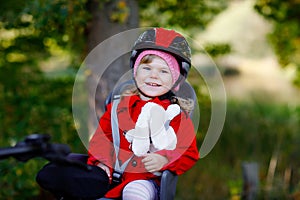 Little toddler girl with security helmet on head sitting in bike seat of her mother or father bicycle. Safe and child