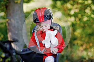 Little toddler girl with security helmet on head sitting in bike seat of her mother or father bicycle. Safe and child