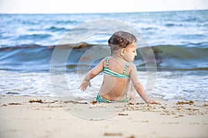 Little toddler girl sitting on the beach and looking at the waves. back view