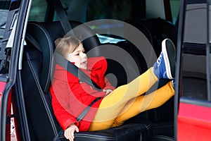 Little toddler girl sitting in car seat and looking out of the window on nature and traffic. Cute kid traveling by car
