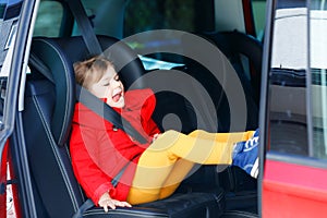 Little toddler girl sitting in car seat and looking out of the window on nature and traffic. Cute kid traveling by car