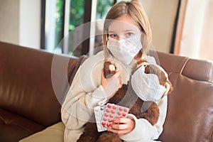 Little toddler girl sitting in medical mask with teddy bear feeling sick with flu and fever