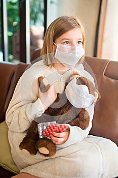 Little toddler girl sitting in medical mask with teddy bear feeling sick with flu and fever