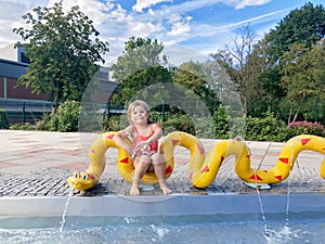 Little toddler girl splashing in an outdoors swimming pool on warm summer day. Happy healthy child enjoying sunny