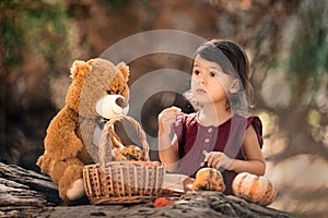 Little toddler girl standing near log with pumpkins and teddy bear in the fall