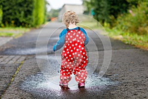 Little toddler girl wearing rain boots and trousers and walking during sleet, rain on cold day. Baby child having fun