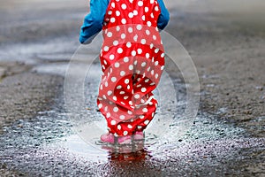 Little toddler girl wearing rain boots and trousers and walking during sleet, rain on cold day. Baby child having fun