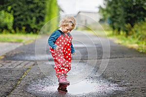 Little toddler girl wearing rain boots and trousers and walking during sleet, rain on cold day. Baby child having fun