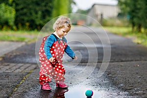 Little toddler girl wearing rain boots and trousers and walking during sleet, rain on cold day. Baby child having fun