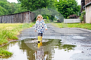 Little toddler girl wearing yellow rain boots, running and walking during sleet on rainy cloudy day. Cute happy child in photo