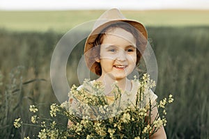 Little toddler girl in a yellow dress walking and picking yellow flowers on a meadow field