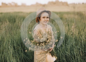Little toddler girl in a yellow dress walking and picking yellow flowers on a meadow field