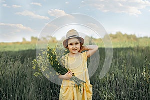 Little toddler girl in a yellow dress walking and picking yellow flowers on a meadow field